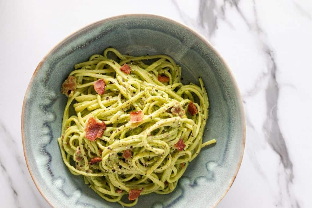 avocado carbonara served in a blue bowl topped with a little bit of extra bacon