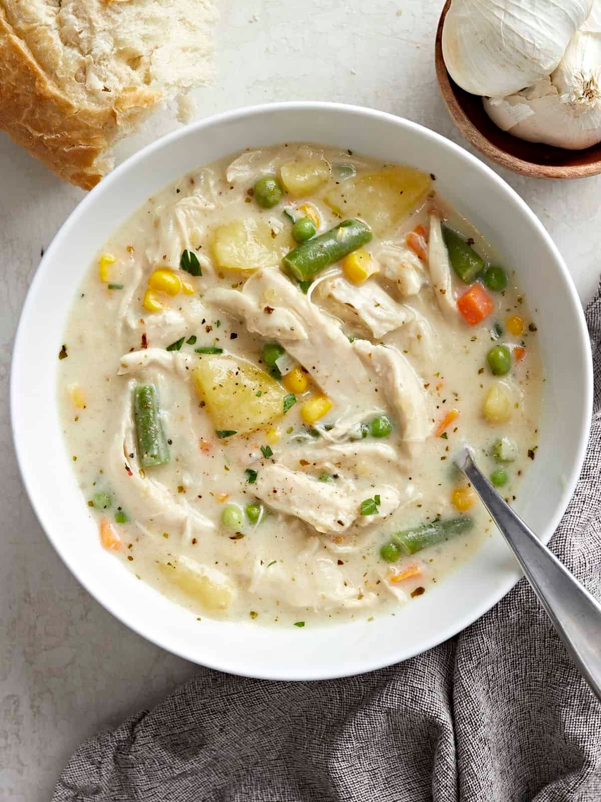 Overhead view of a bowl of chicken pot pie soup with crusty bread on the side and a spoon inside the bowl.