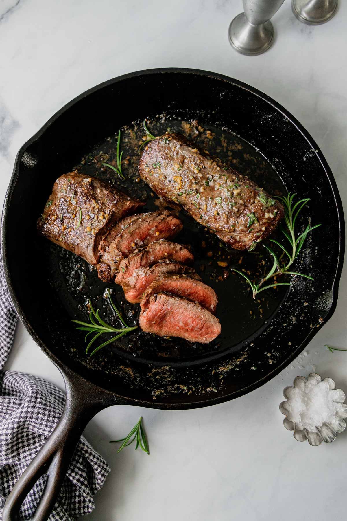 Medium rare seared venison tenderloins are in a cast iron skillet against a white backdrop.