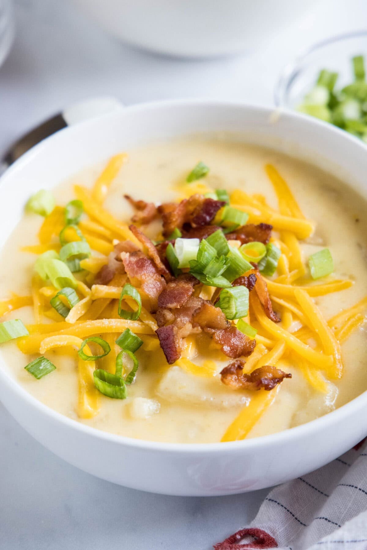 With a creamy broth, hearty chunks of potatoes, gooey cheese, and crispy bacon, this Instant Pot potato soup is the ultimate comfort meal. Close up of a bowl of potato soup with cheese, bacon, and green onions on top.
