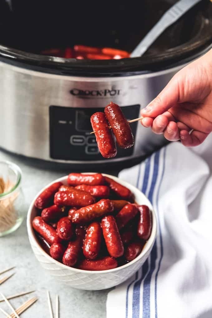 a hand holding a toothpick with two honey garlic little smokies on it