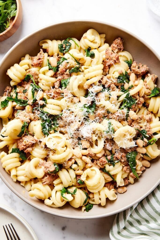 Brown bowl on marble surface filled with weeknight spinach and sausage pasta with Parmesan cheese sprinkled on top.