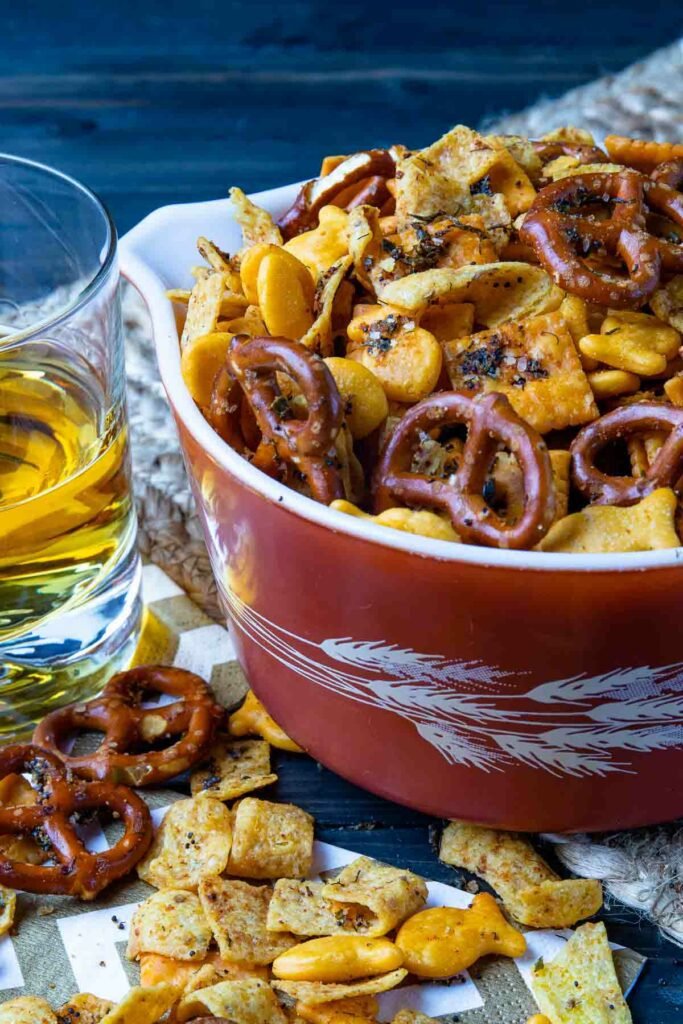 Spicy Cheese Cracker Snack Mix in a bowl with a drink for appetizers.