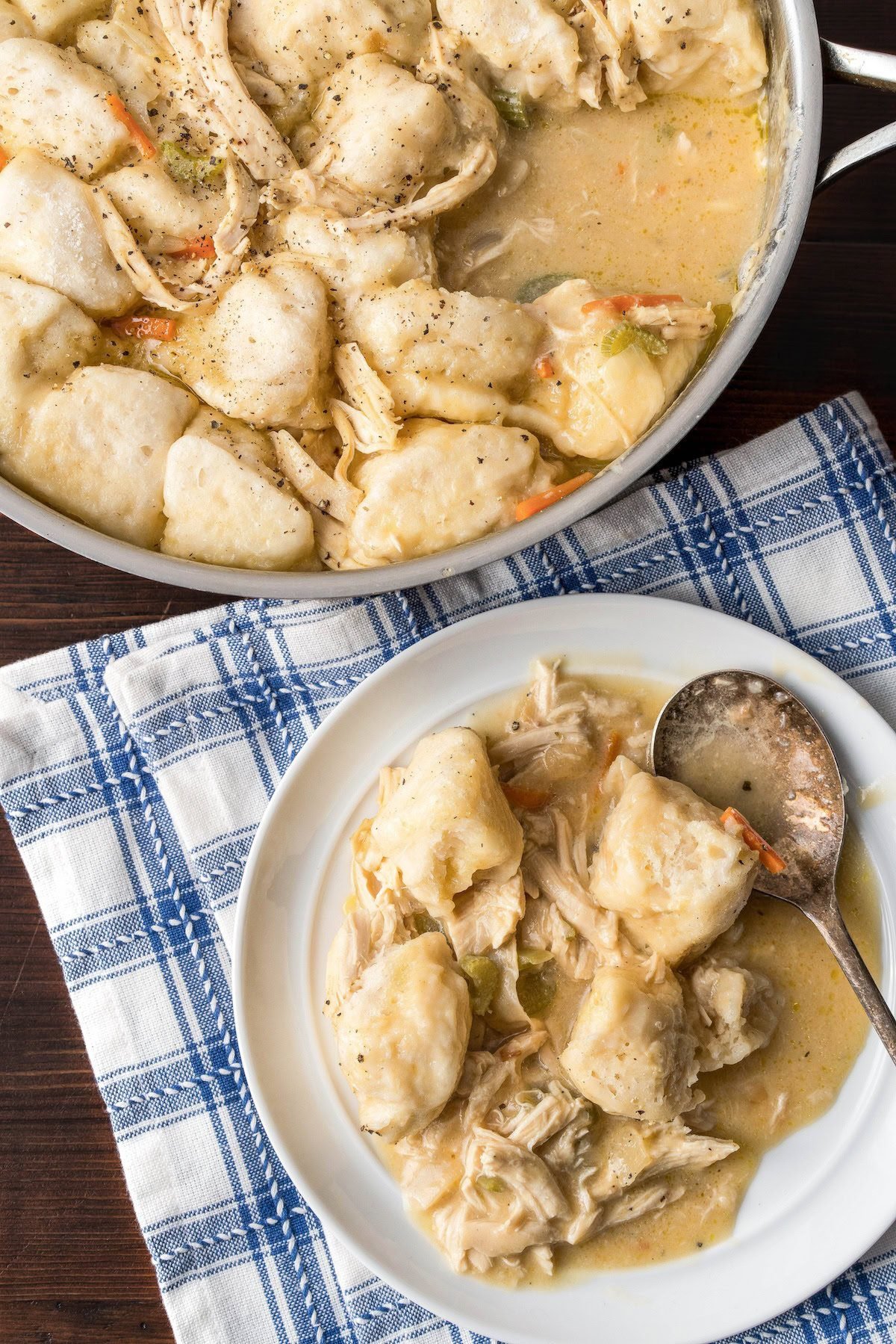 A pot filled with easy chicken and dumplings with biscuits with a bowl filled with dumplings and a spoon on the side.