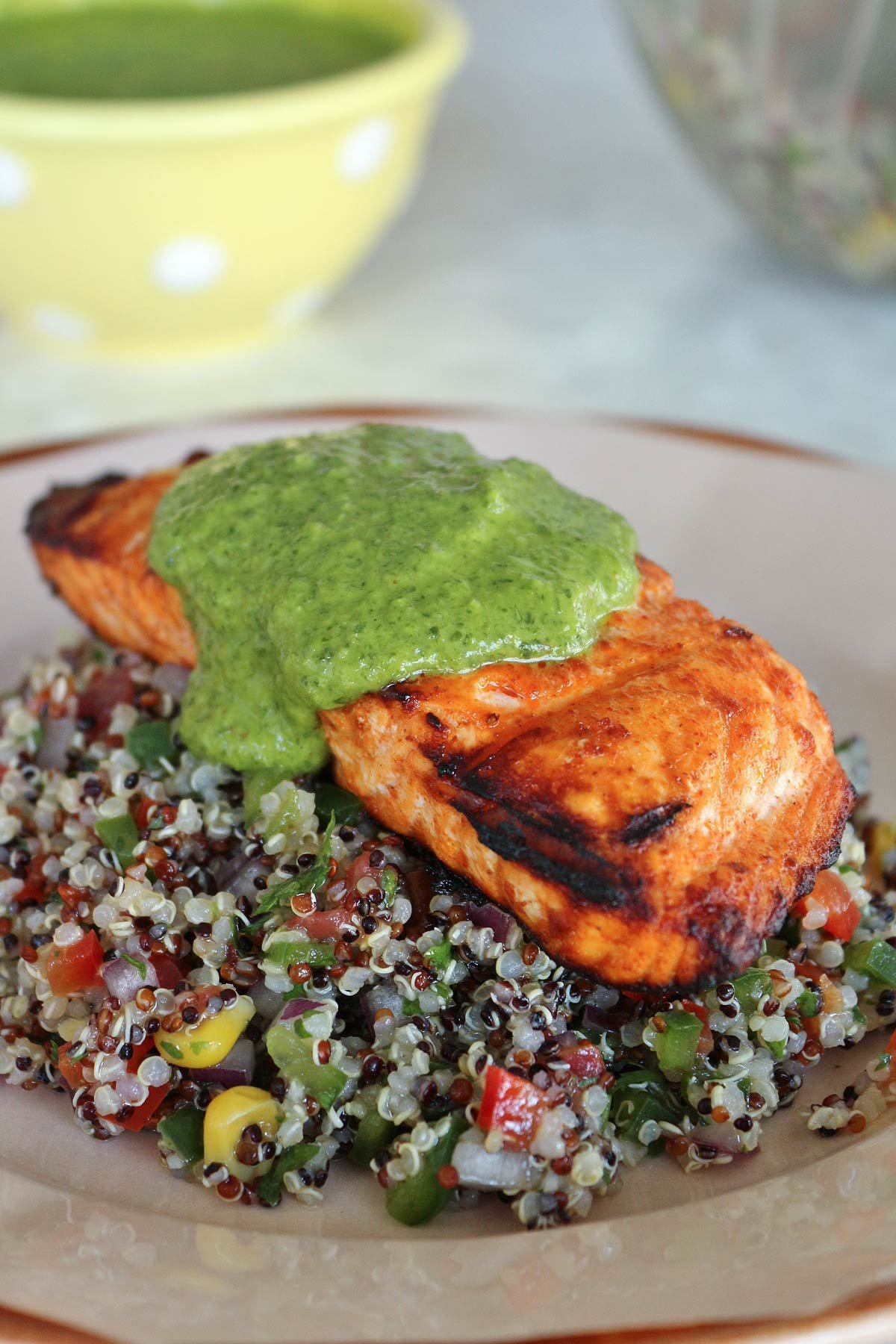 A grilled salmon fillet on a bed of quinoa salad topped with bright green sauce.