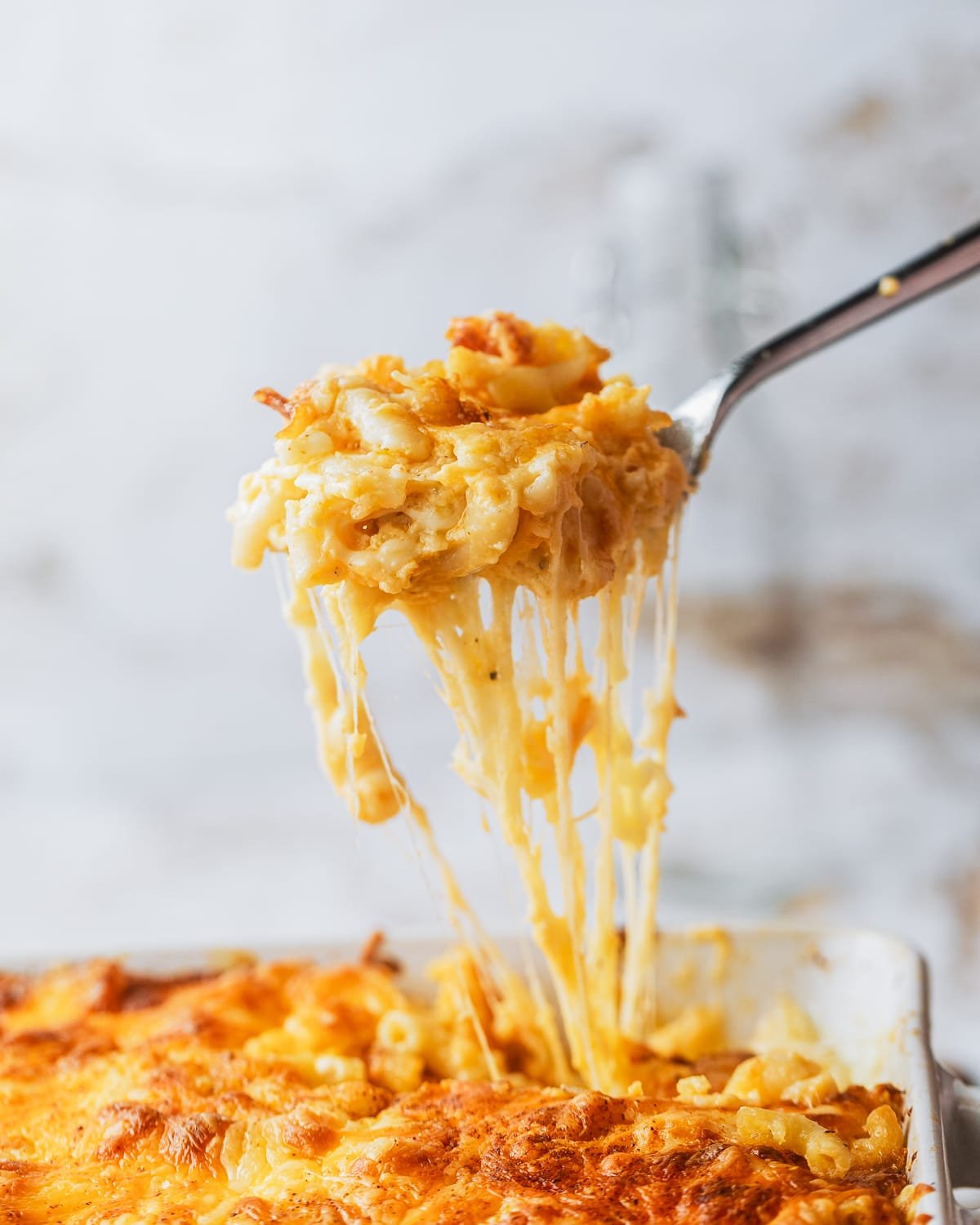 a spoonful of soul food southern baked mac and cheese being lifted from the pan with a big cheese pull