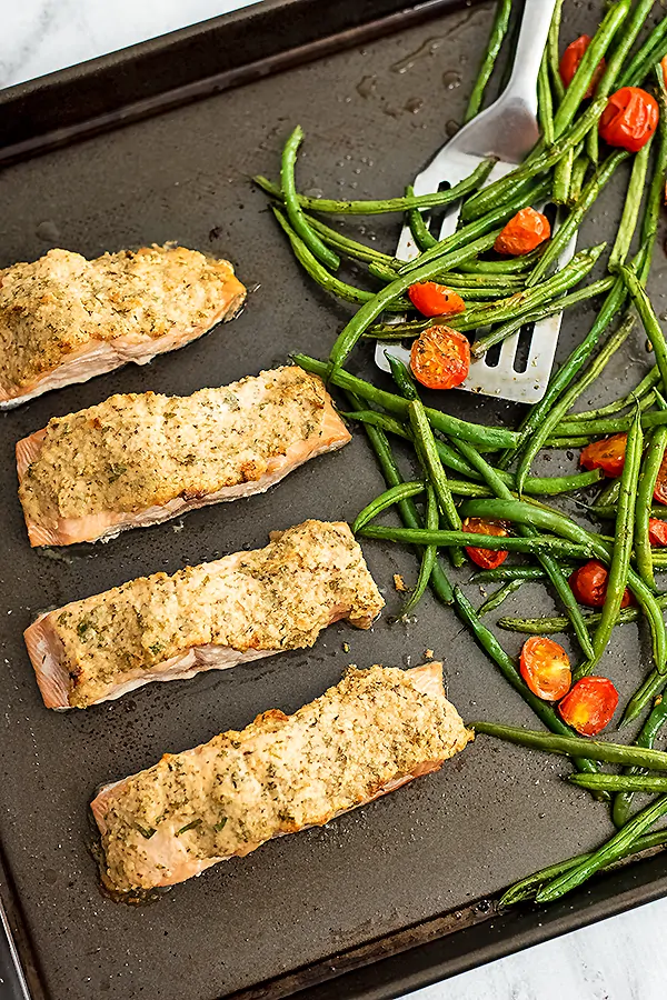 Sheet pan with tahini herb crusted salmon and green beans and tomatoes.