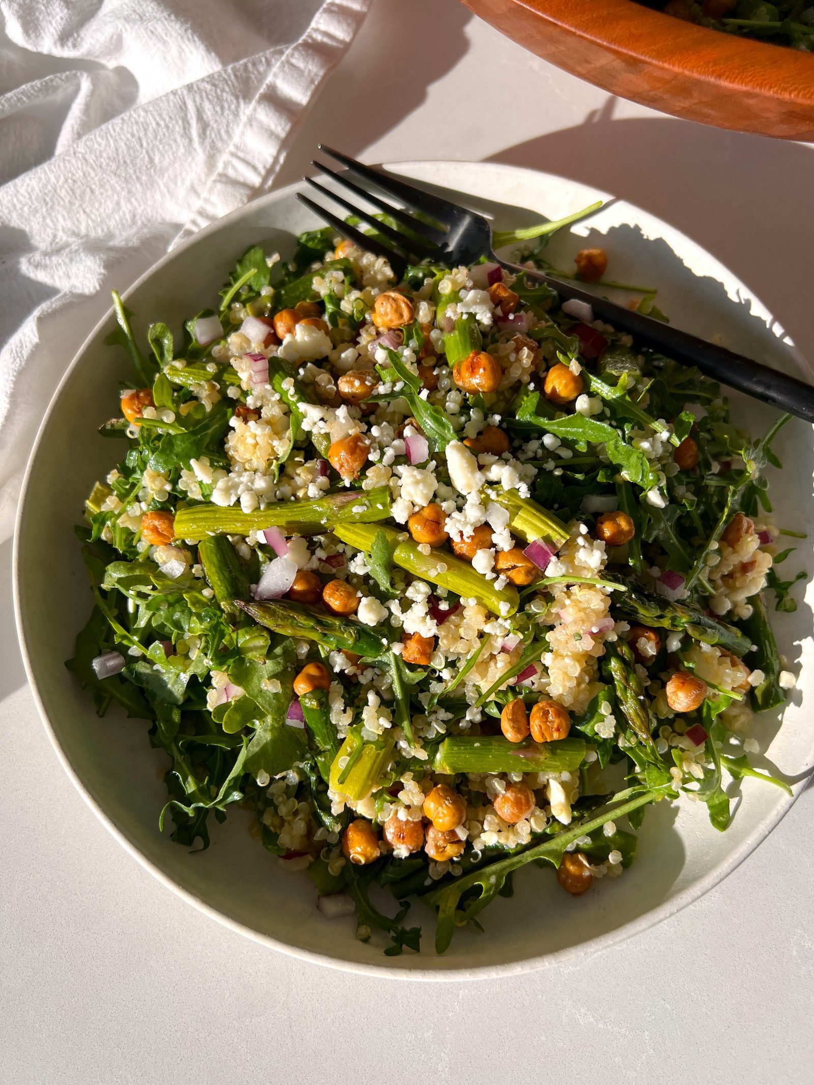 Spring Arugula and Quinoa Salad with Lemon Dressing on white plate with black fork and salad bowl in the background