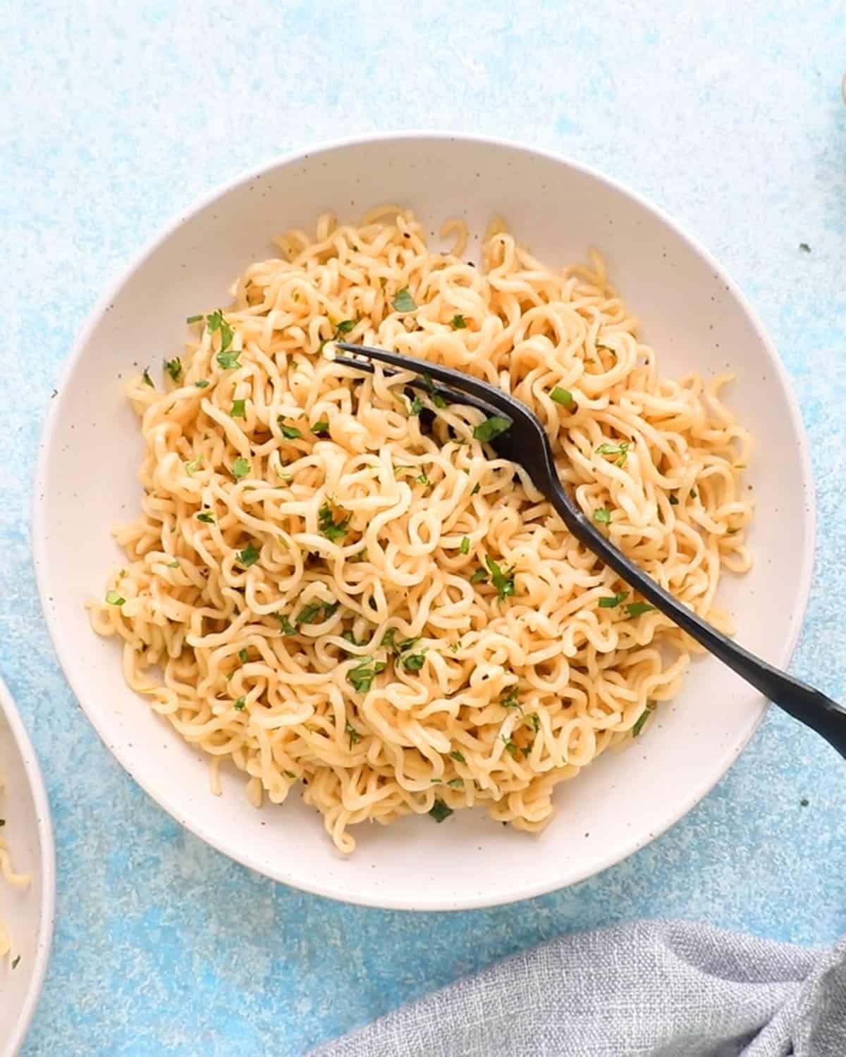 white buttered noodles in a round white plate along with a black fork.