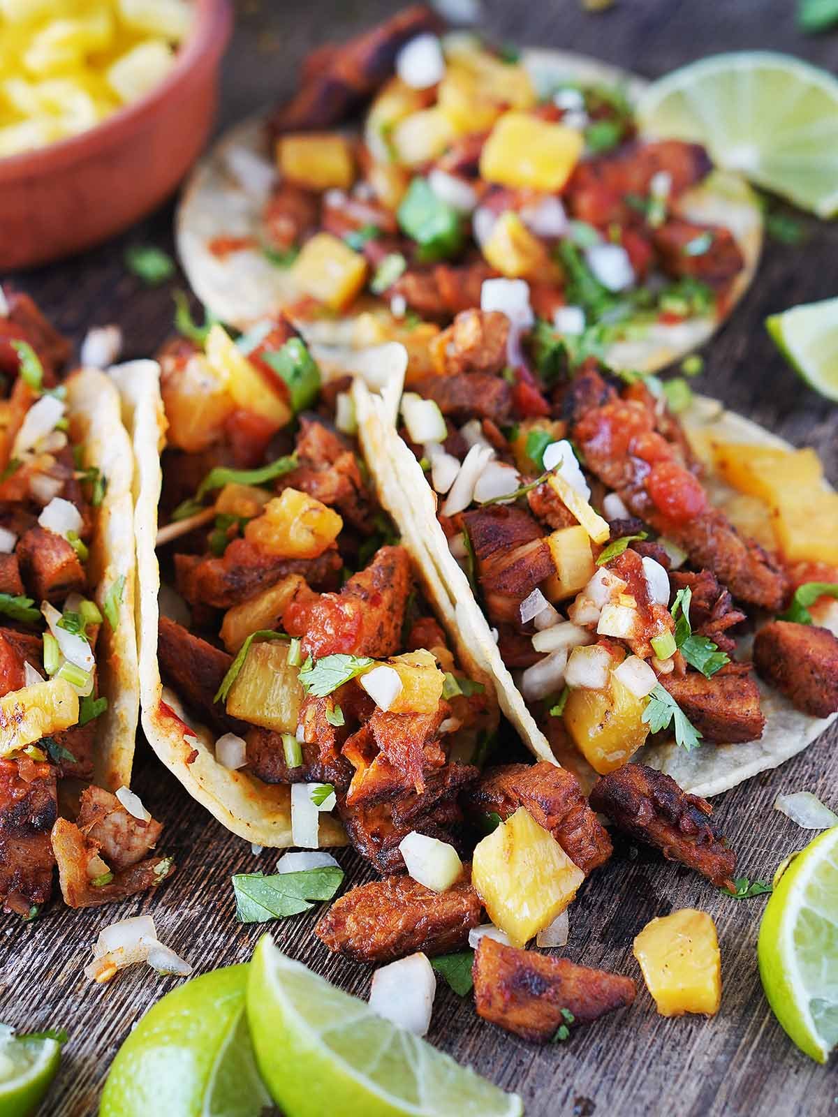 Four tacos al pastor on a wood board.