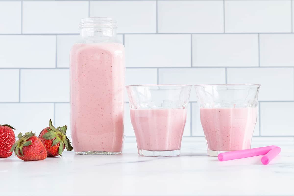strawberry smoothie in jar and cups on counter