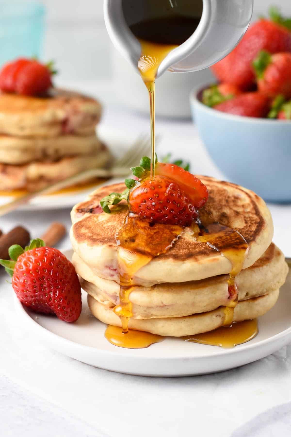 Strawberry Pancakes stacked on a table and decorated with fresh strawberries.