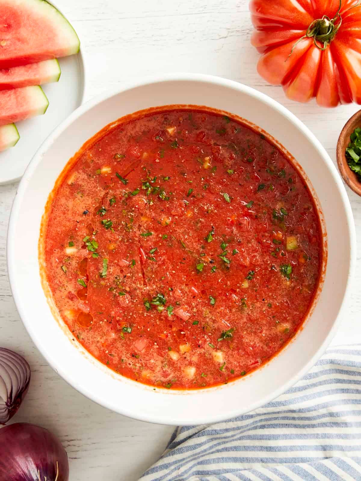 overhead view of watermelon gazpacho in a white bowl with minced fresh herbs.