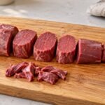 Beef tenderloin portions arranged on a wooden board, including steaks, roasting pieces and trimmings.